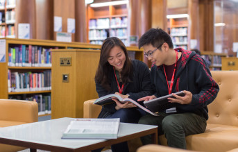 two people sitting on a sofa in a library reading a book together