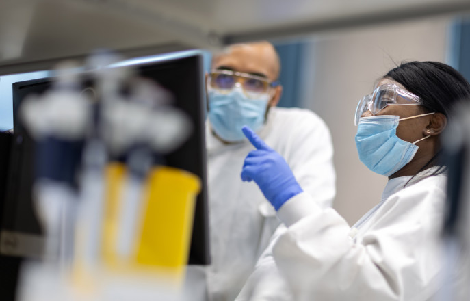 Researchers in the lab wearing PPE look at a screen
