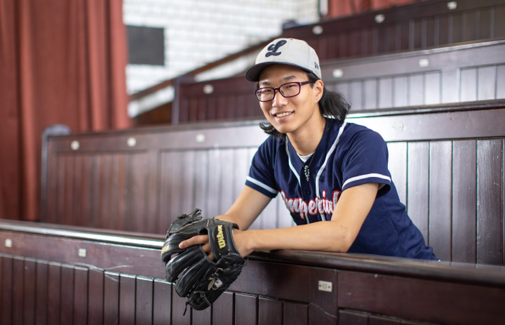 Ben Shin in a lecture theatre, wearing a baseball kit and glove