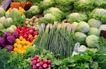 An abundance of bright vegetables piled up on an outdoor market stall, including bunches of radishes, spring onions, cabbages, lettuces and potates. Photo by Mordo Bilman on Unsplash.